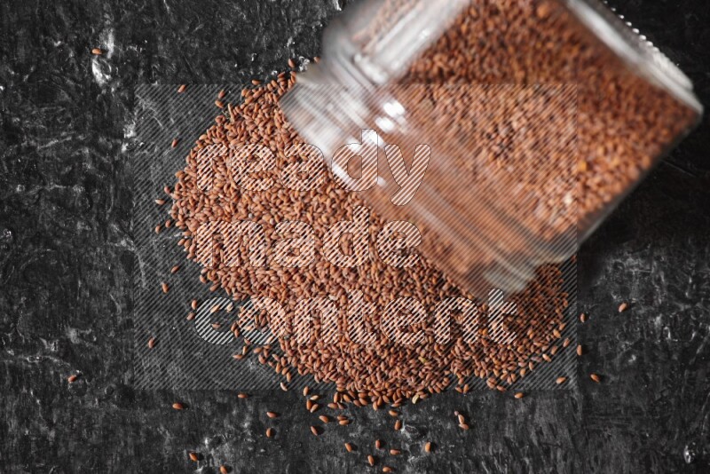 وعاء زجاجي مقلوب ممتلئ ببذور حب الرشاد وتناثرت البذور منه على أرضية سوداء