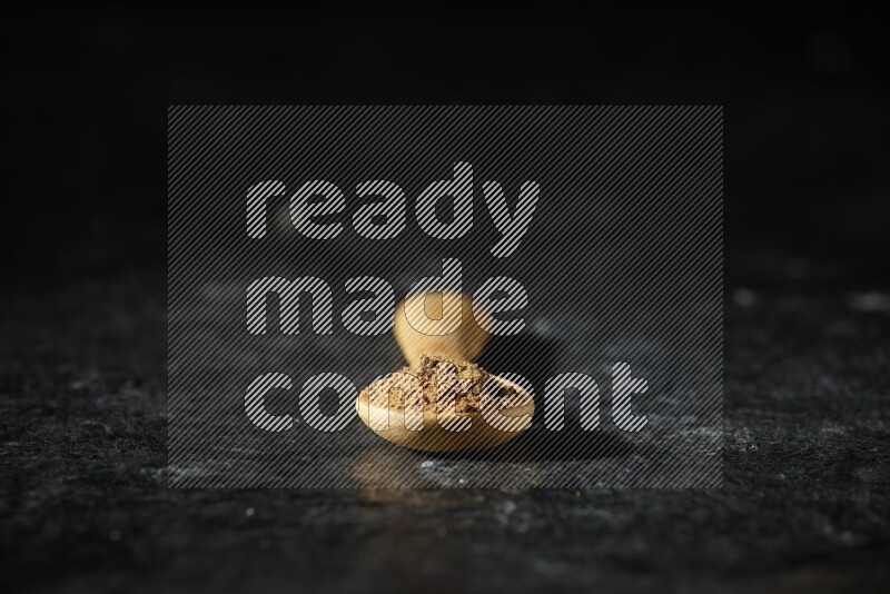 A wooden spoon full of allspice powder on a textured black flooring