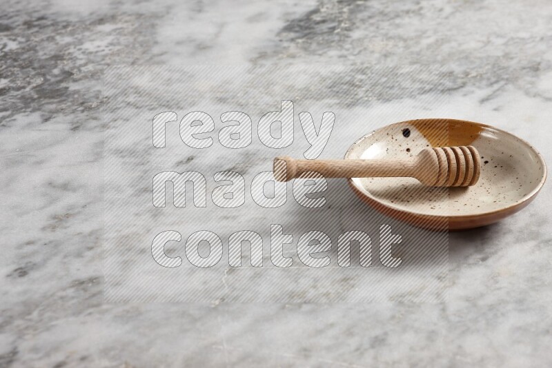 Multicolored pottery plate with wooden honey dipper in it on grey marble background