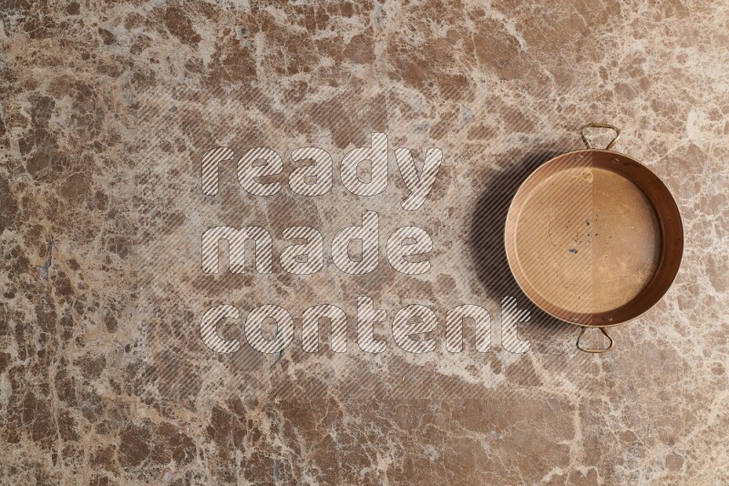 A small copper pan on beige marble background