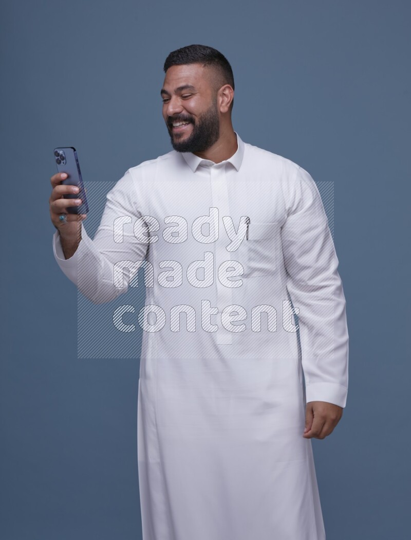 A man Texting on Blue Background wearing Saudi Thob