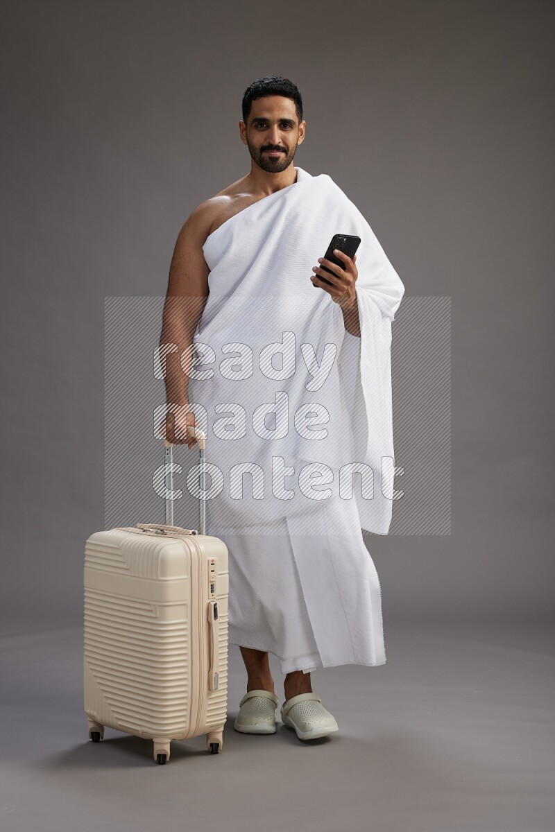 A man wearing Ehram Standing holding traveling bag on gray background