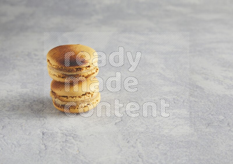 45º Shot of two Yellow Crème Brulée macarons on white  marble background