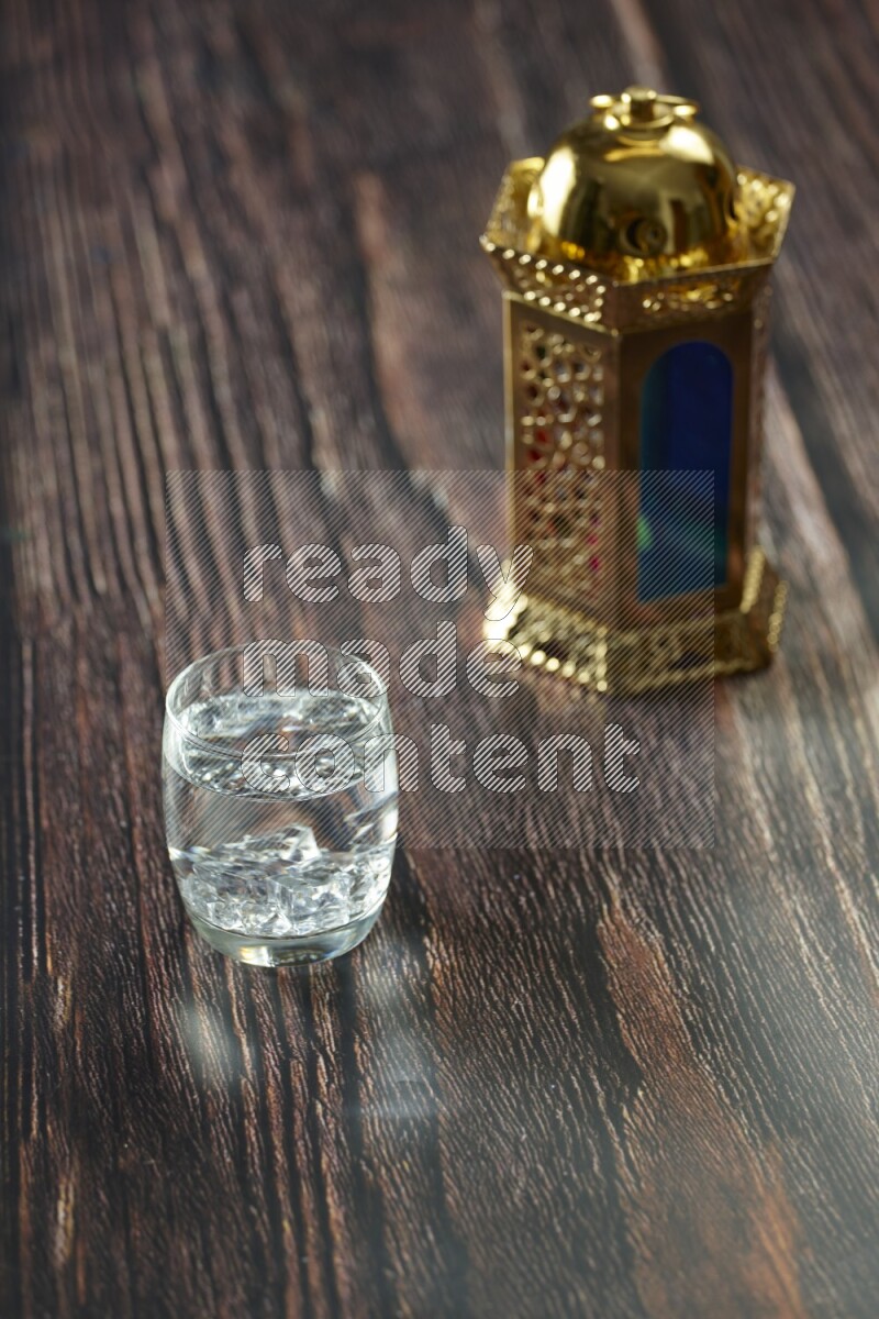 A golden lantern with different drinks, dates, nuts, prayer beads and quran on brown wooden background