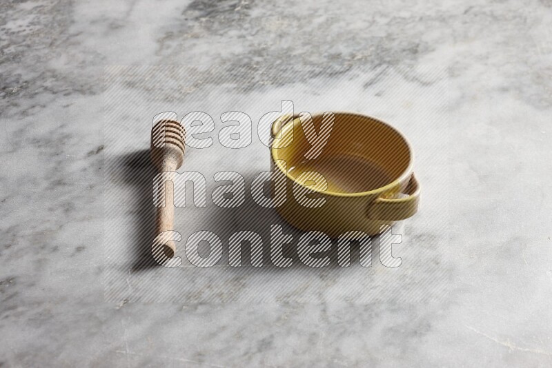 Multicolored pottery bowl with wooden honey dipper on the side on grey marble background