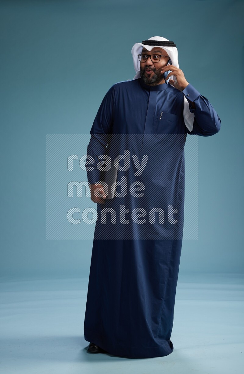 Saudi Man with shimag Standing talking on phone on blue background