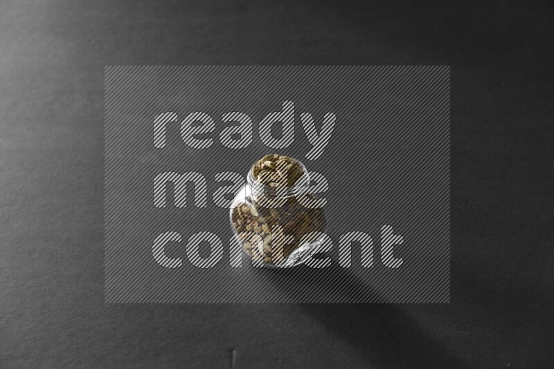 A glass spice jar full of cardamom on black flooring