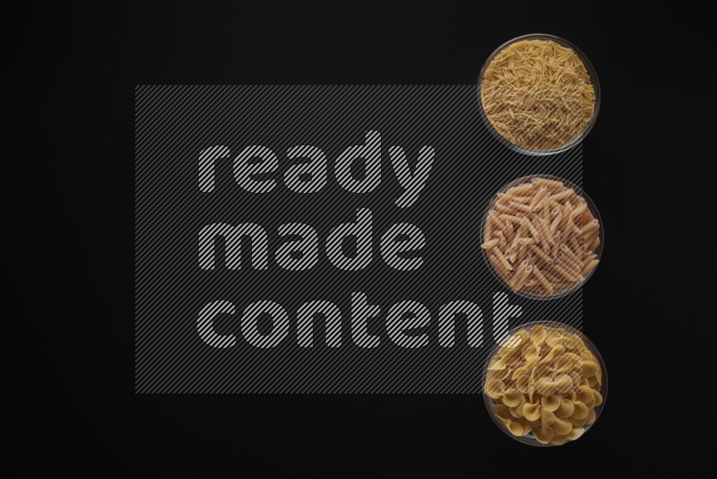Different pasta types in 3 glass bowls on black background