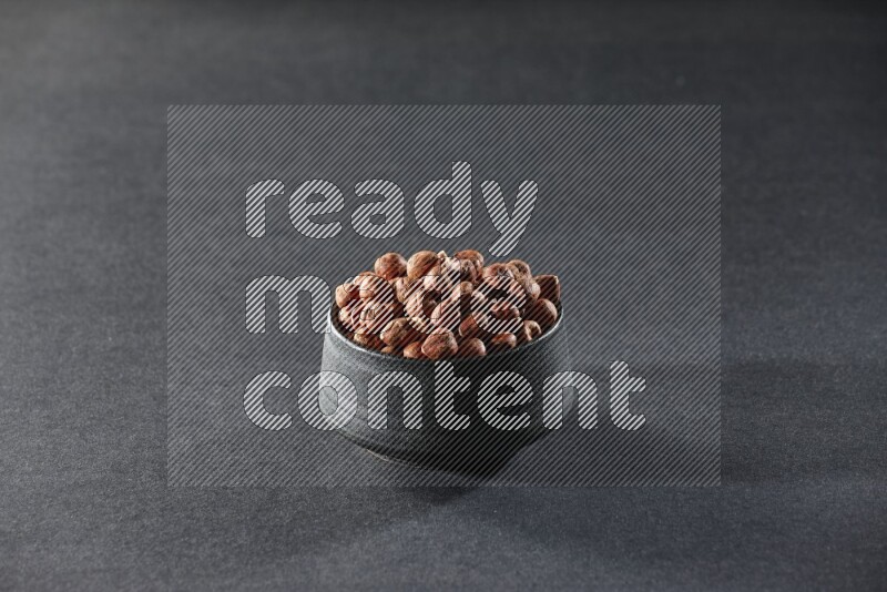 A black pottery bowl full of peeled hazelnuts on a black background in different angles
