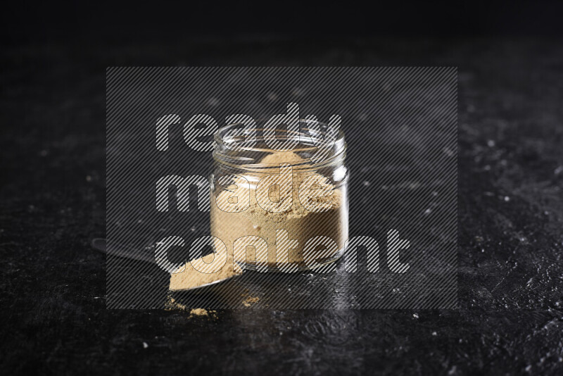 A glass jar full of ground ginger powder on black background