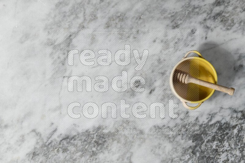 Multicolored pottery bowl with wooden honey dipper in it on grey marble background