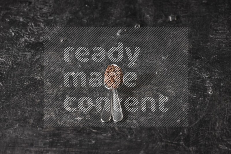 ملعقتان معدنيتان ممتلئتان بحبوب بذر الكتان علي خلفية سوداء