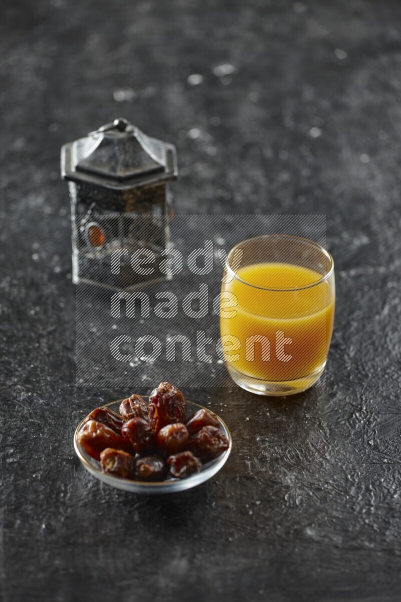 A silver lantern with different drinks, dates, nuts, prayer beads and quran on textured black background