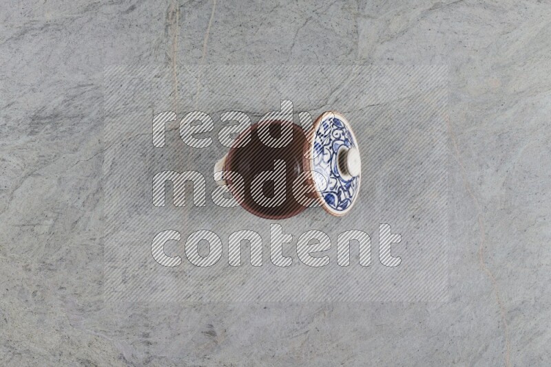 A multicolored pottery pot with its lid on grey marble background