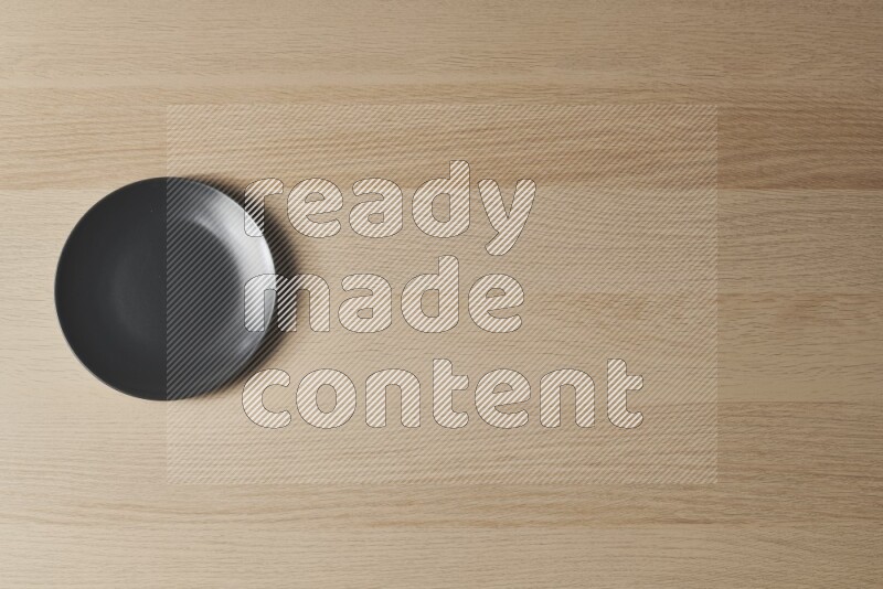A black ceramic circular plate on light wooden background