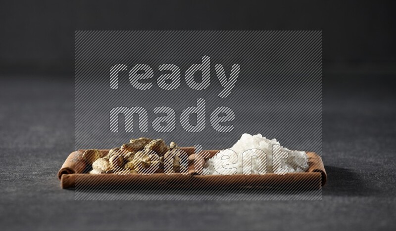 2 squares of cinnamon sticks full of white salt and turmeric fingers on black flooring