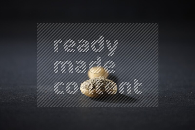 A wooden spoon full of cardamom powder on black flooring