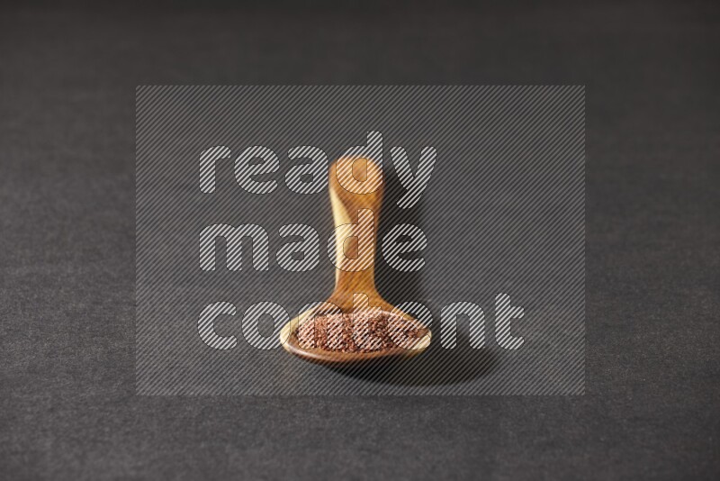 A wooden ladle full of garden cress seeds on a black flooring