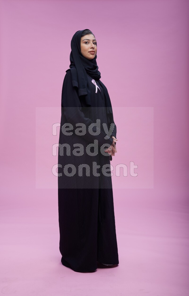 Saudi woman wearing Abaya standing with crossed arms on pink background
