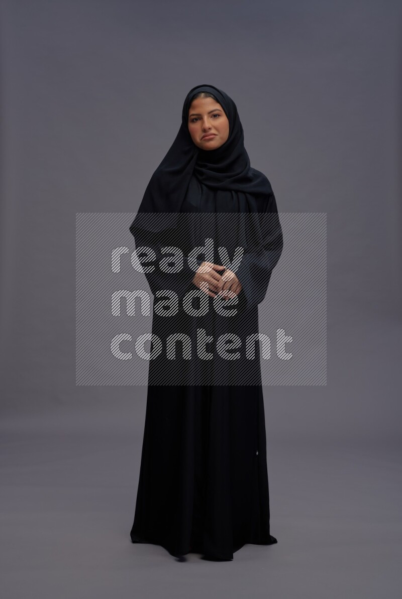 Saudi woman wearing Abaya standing interacting with the camera on gray background