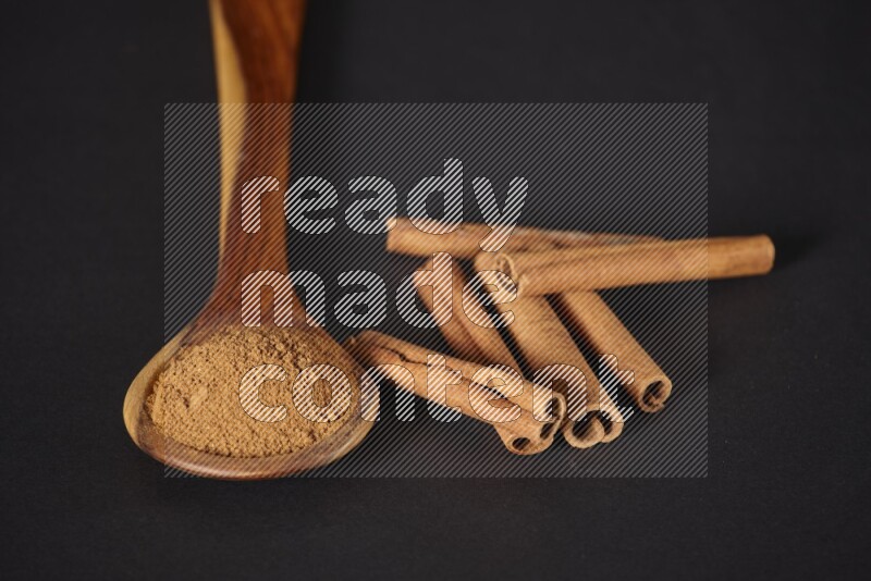 Cinnamon powder in a wooden ladle spoon beside it cinnamon sticks on the flooring on black background in different angles