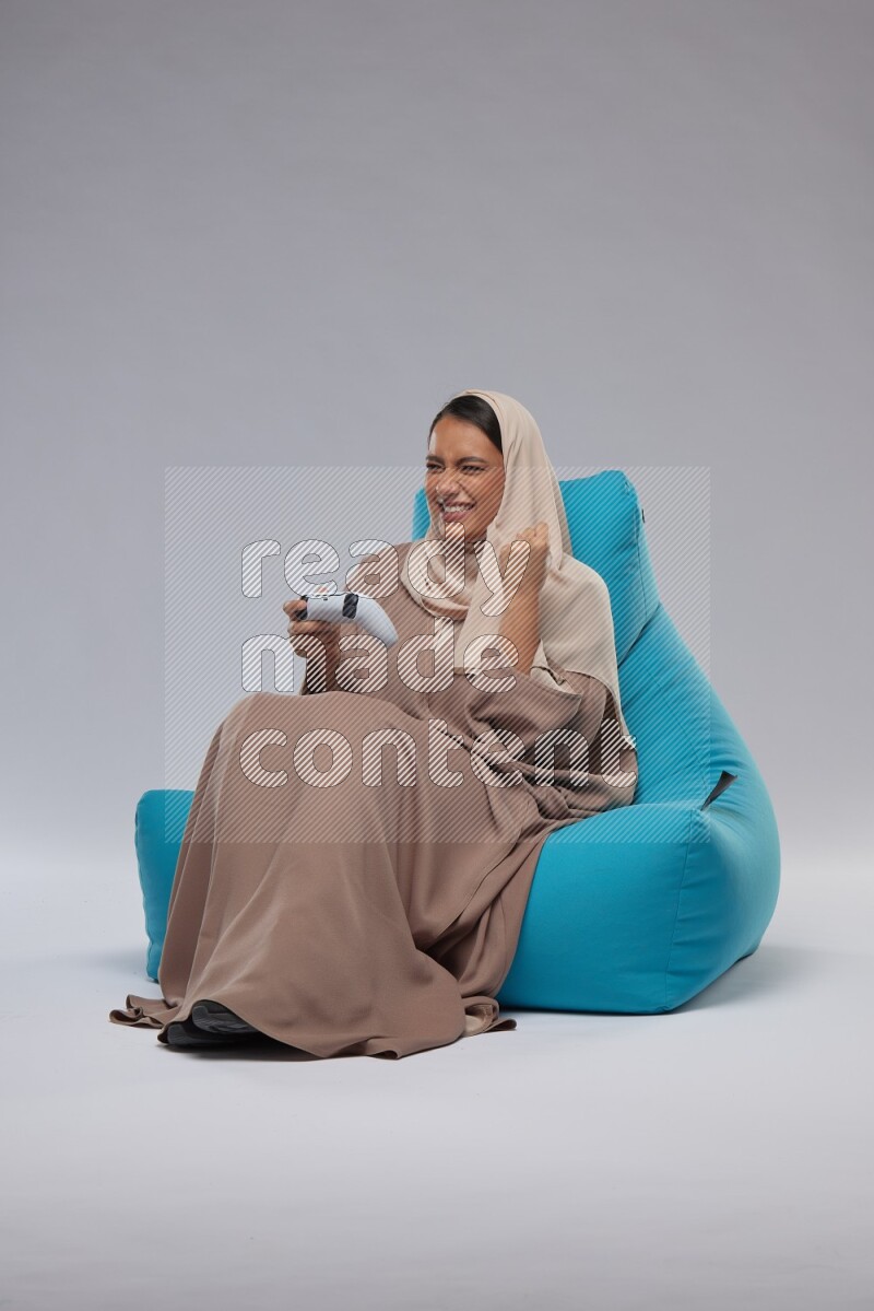A Saudi woman sitting on a blue beanbag and gaming with joystick