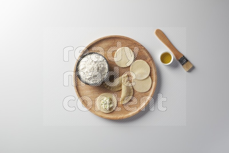 two closed sambosas and one open sambosa filled with cheese while flour, and oil with oil brush aside in a wooden dish on a white background