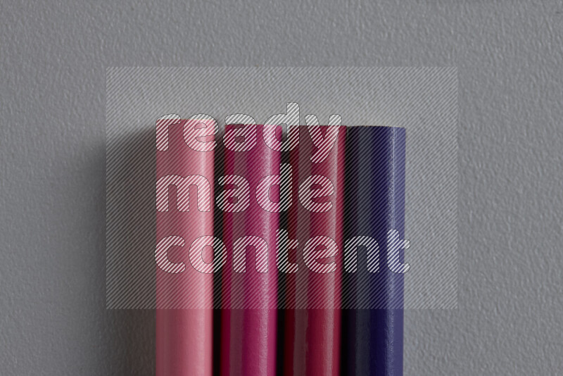 A collection of sharpened colored pencils arranged showcasing a gradient of pink and purple hues on grey background