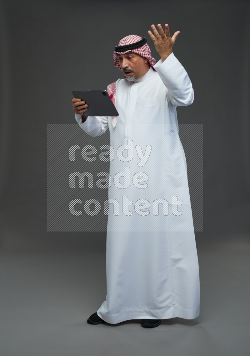 Saudi man with shomag Standing working on tablet on gray background