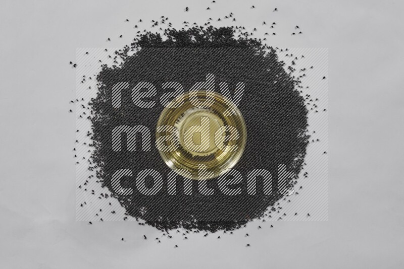 A glass bowl full of black seeds oil surrounded by the seeds on a white flooring