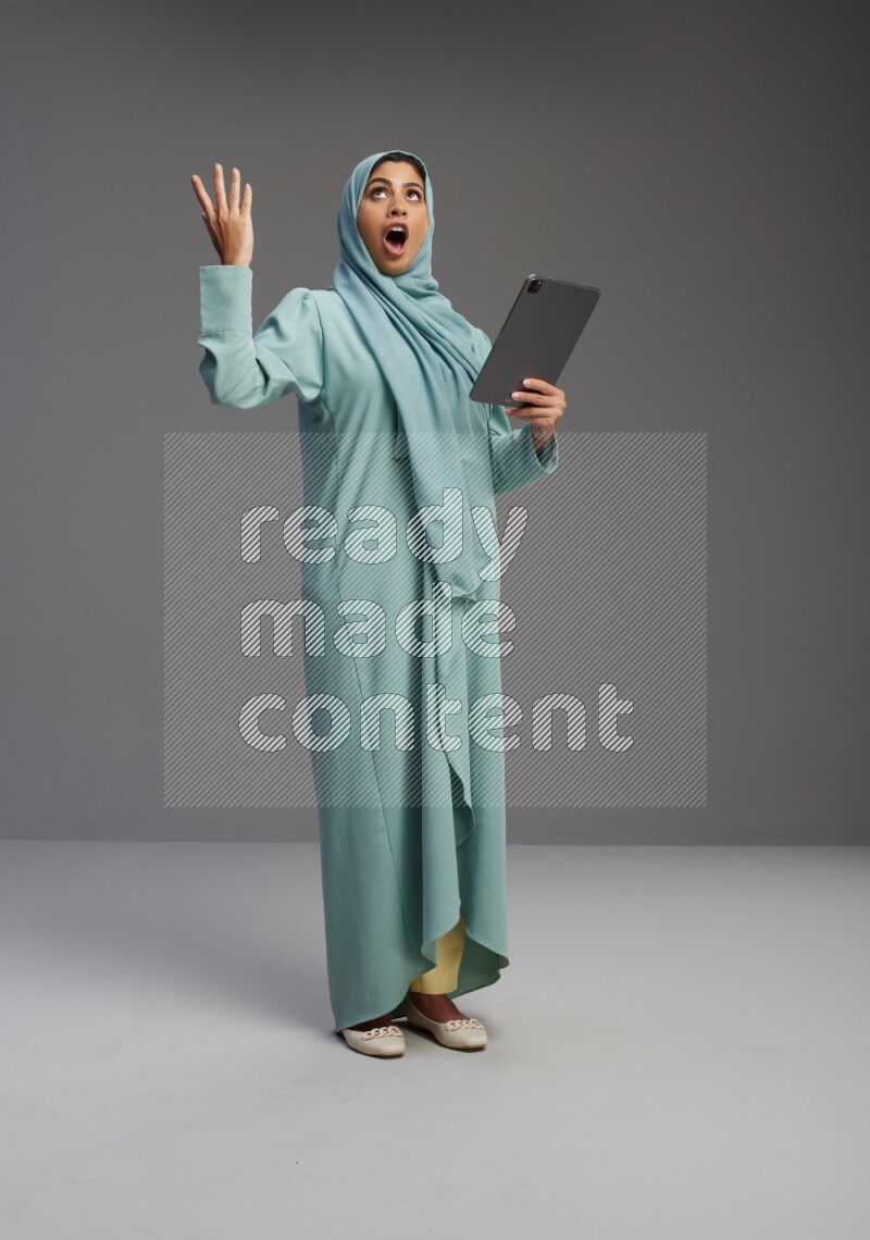 Saudi Woman wearing Abaya standing working on tablet on Gray background