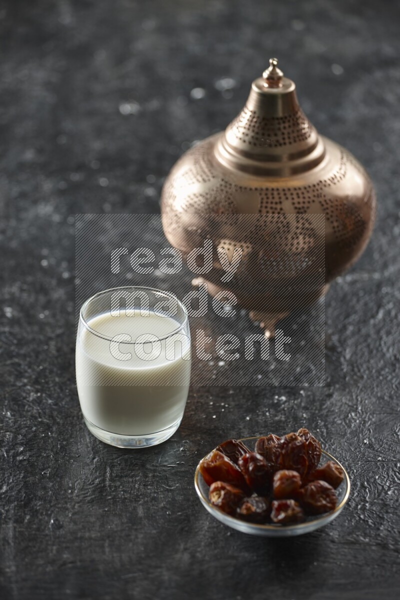 A golden lantern with different drinks, dates, nuts, prayer beads and quran on textured black background