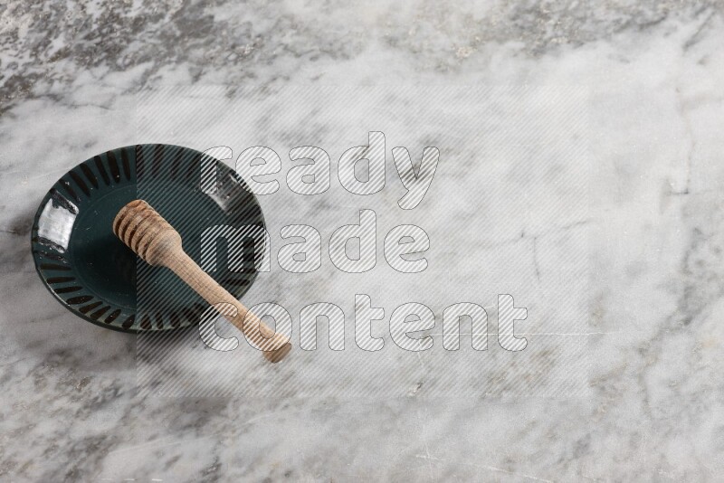 Multicolored pottery plate with wooden honey dipper in it on grey marble background