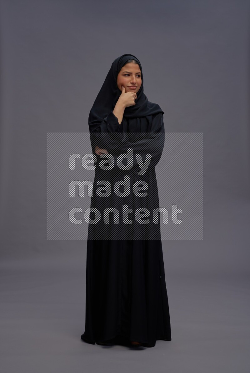 Saudi woman wearing Abaya standing interacting with the camera on gray background