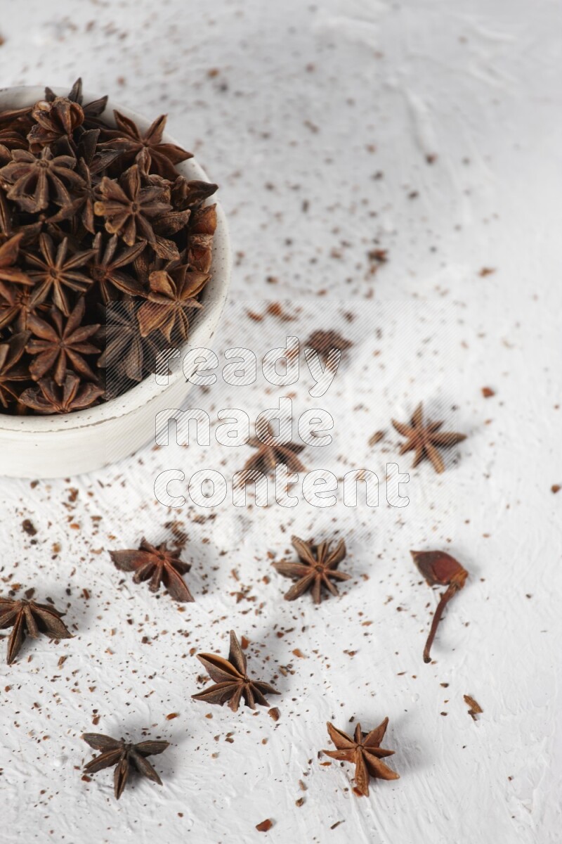 Star Anise in a white bowl and more of it sprinkled on white background