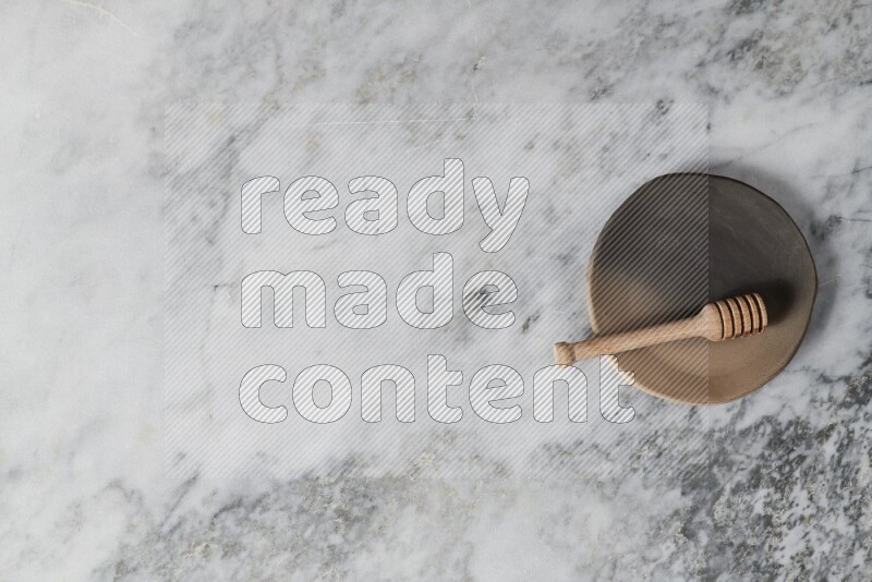 طبق فخاري متعدد الألوان مع ملعقة عسل خشبية بداخله على خلفية من الرخام الرمادي