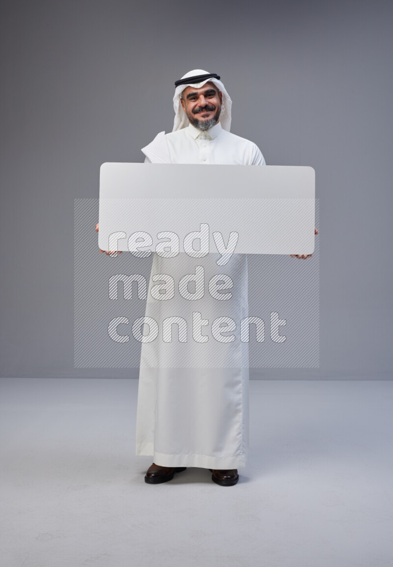 Saudi man Wearing Thob and white Shomag standing holding board on Gray background