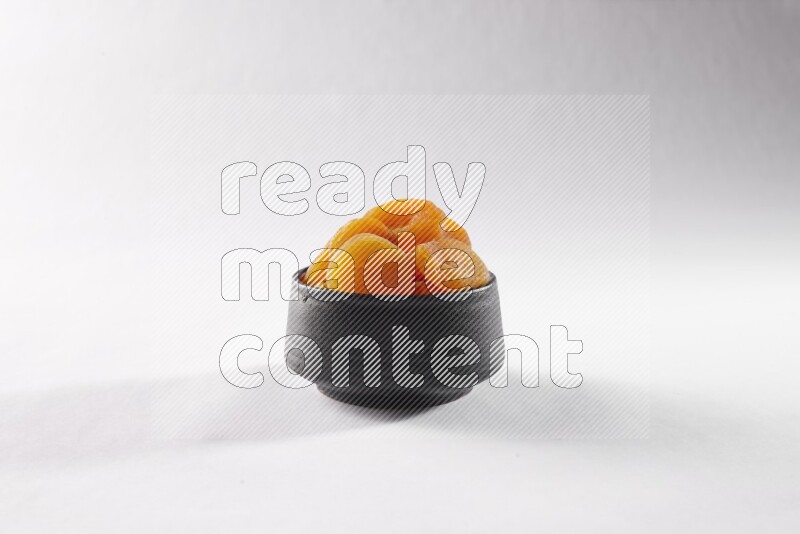Dried apricots in a black pottery bowl on white background
