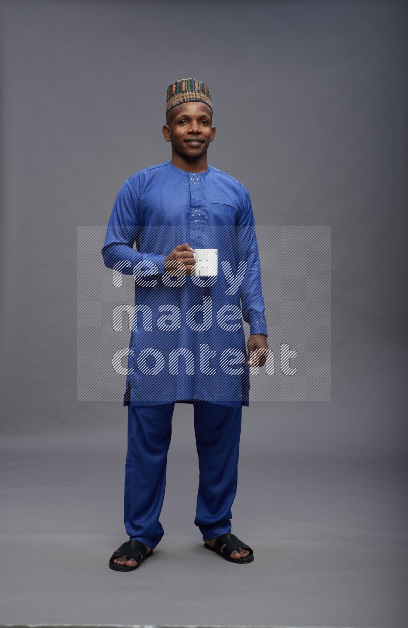 Man wearing Nigerian outfit standing holding mug on gray background