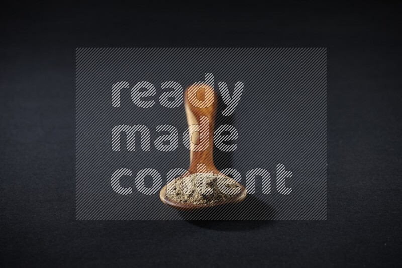 مغرفة خشبية ممتلئة ببودرة الهيل على خلفية سوداء