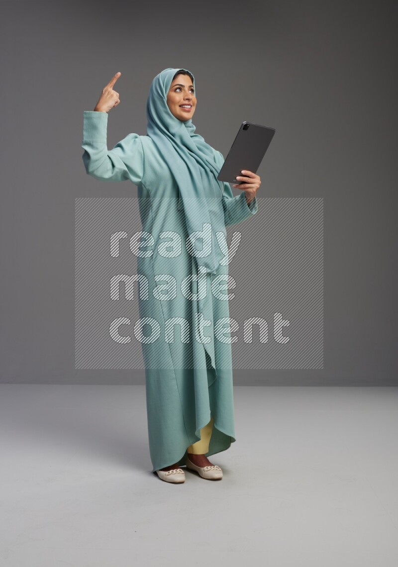 Saudi Woman wearing Abaya standing working on tablet on Gray background