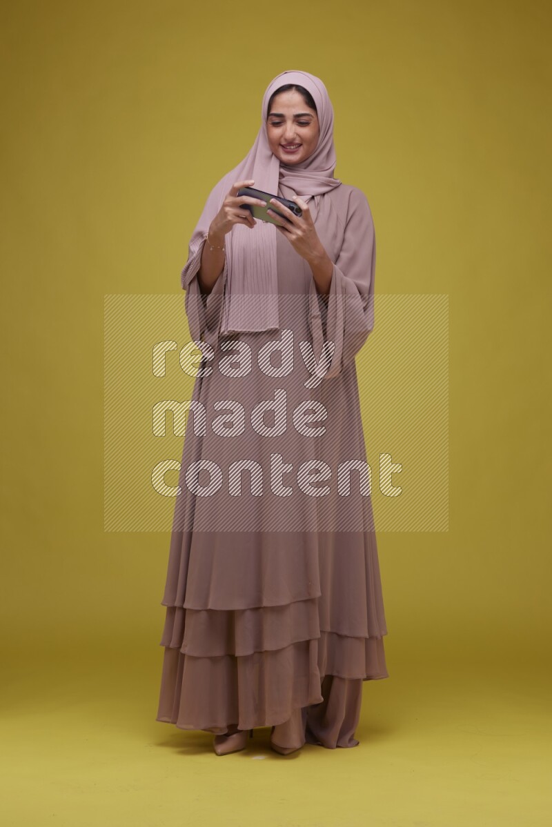 A woman Playing Games a Yellow Background wearing Brown Abaya with Hijab