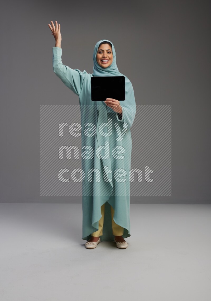 Saudi Woman wearing Abaya standing showing tablet to camera on Gray background