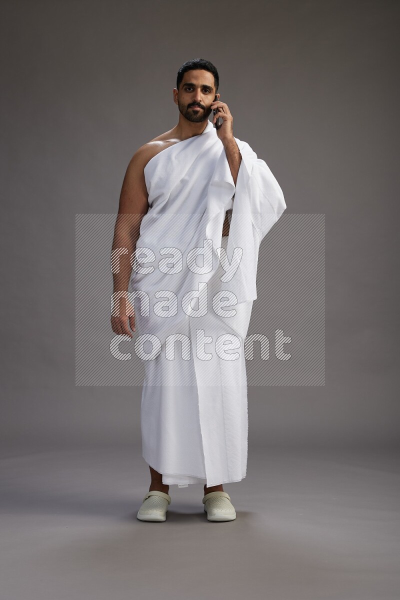 A man wearing Ehram Standing talking on phone on gray background
