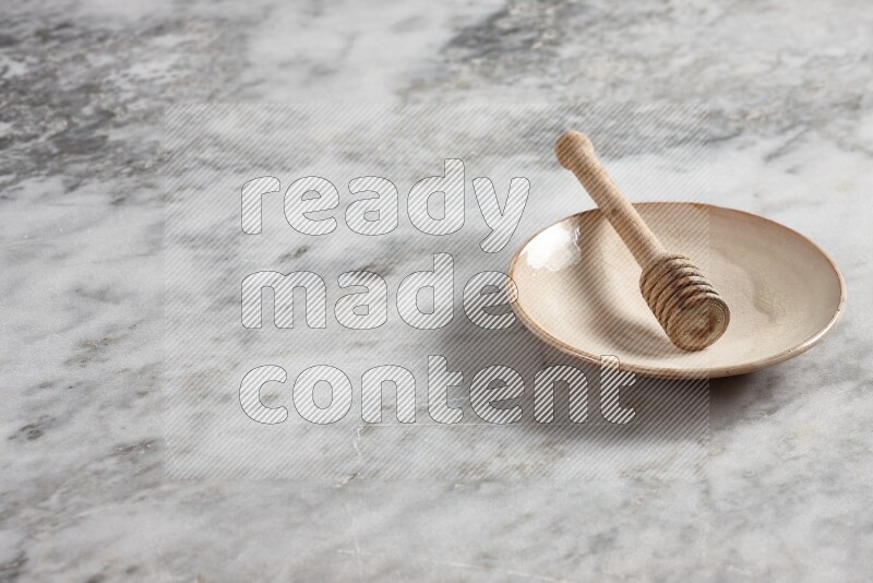 Beige pottery plate with wooden honey dipper in it on grey marble background