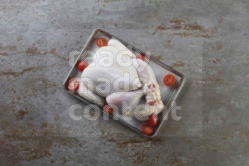 whole Raw chicken on a small oven trey direct on a rustic grey background