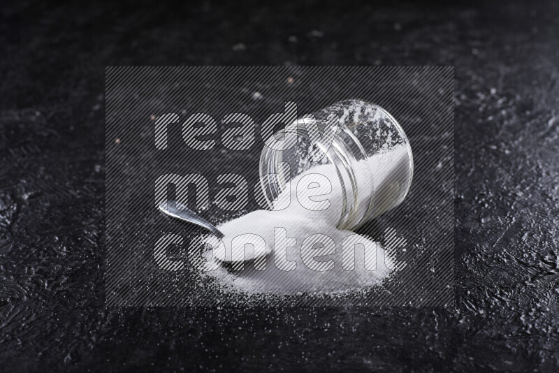 A glass jar full of fine table salt on black background