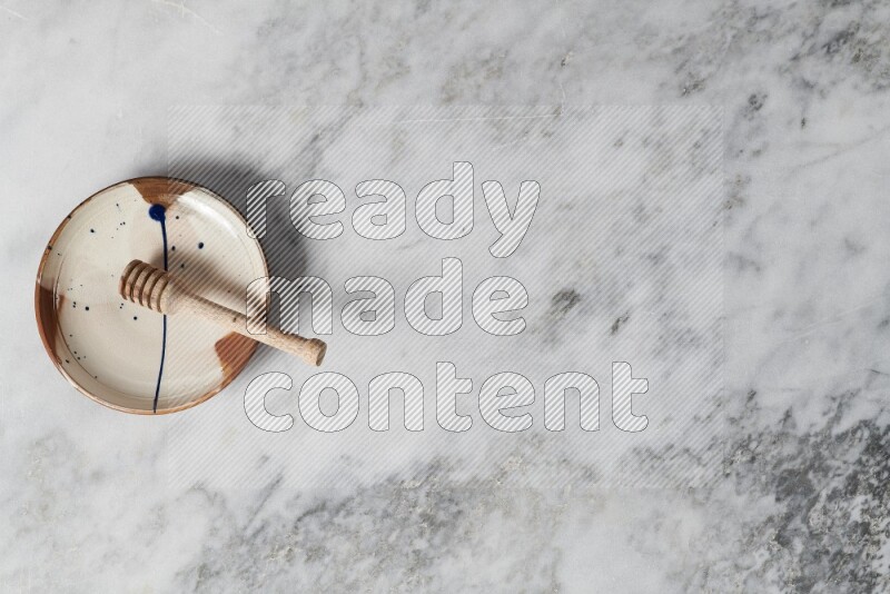 طبق فخاري متعدد الألوان مع ملعقة عسل خشبية بداخله على خلفية من الرخام الرمادي