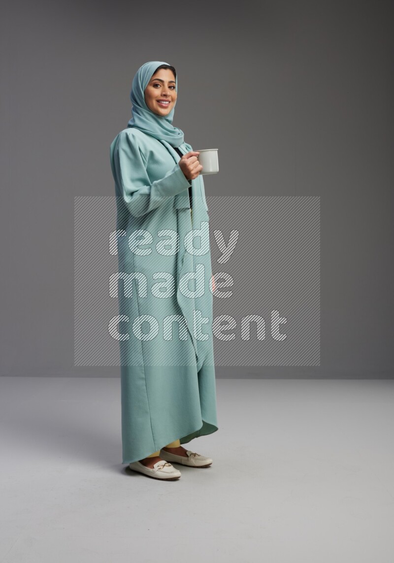 Saudi Woman wearing Abaya standing  holding a mug on Gray background