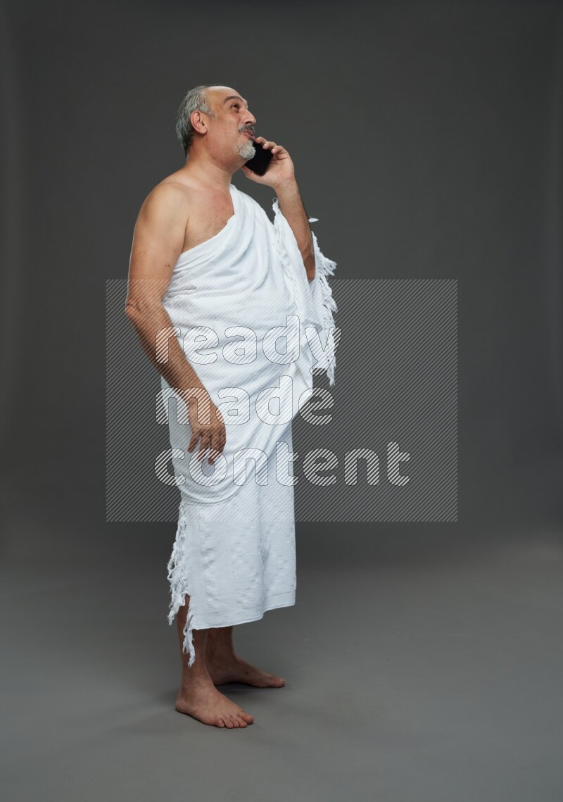 A man wearing Ehram Standing talking on phone on gray background